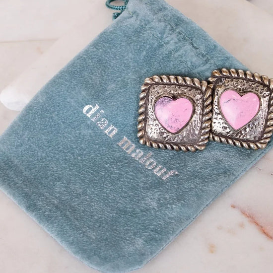 Pair of earrings with pink heart centers on a blue velvet pouch with 'Dian Malouf' branding.