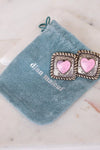 Pair of earrings with pink heart centers on a blue velvet pouch with 'Dian Malouf' branding.