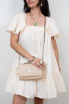 Woman wearing a white dress holding a beige handbag against a plain background