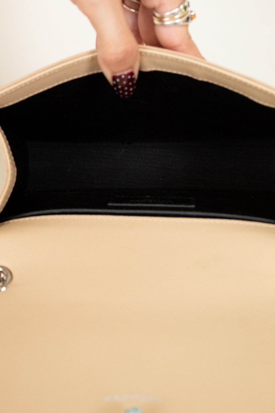 Close-up of a beige handbag with a hand holding it open, showing the interior.