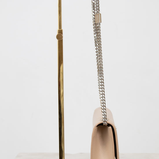 Beige handbag with a chain strap on a gold stand against a white background
