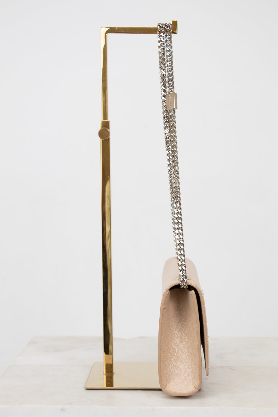 Beige handbag with a chain strap on a gold stand against a white background