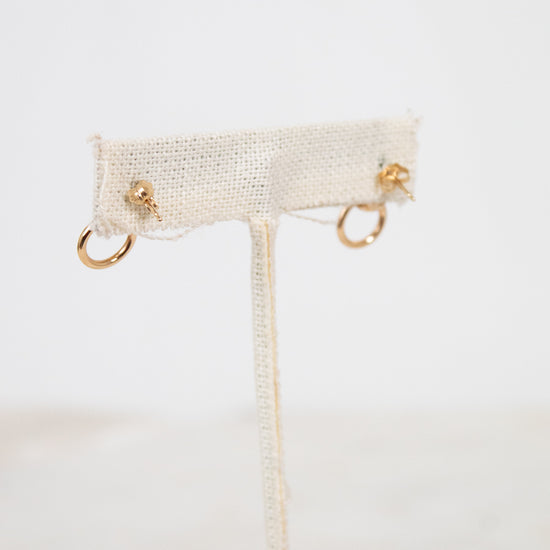 Gold earrings on a white earring stand with a blurred background
