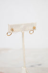 Gold earrings on a white earring stand with a blurred background