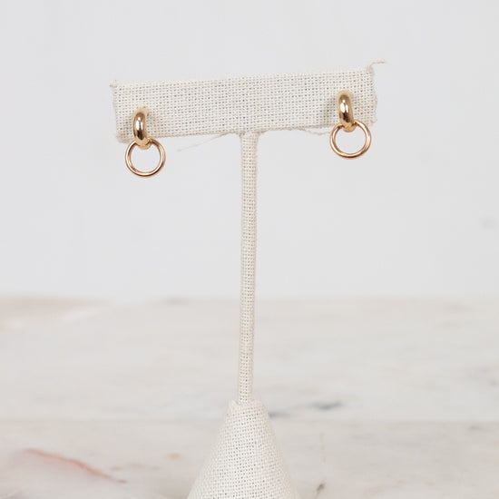 Gold hoop earrings on a textured white earring stand against a light background