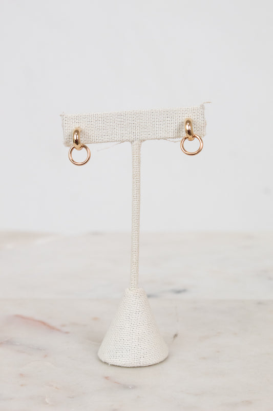 Gold hoop earrings on a textured white earring stand against a light background