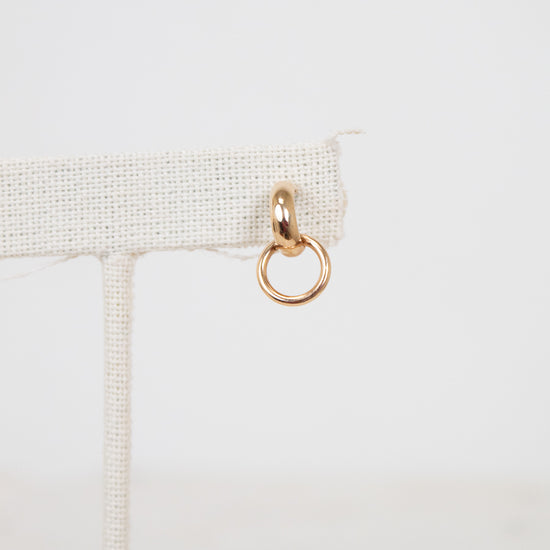 Gold ring hanging from a beige fabric strip on a light gray background