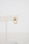 Gold ring hanging from a beige fabric strip on a light gray background