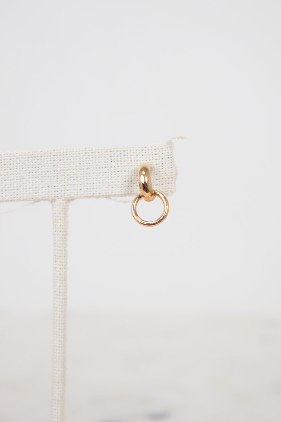 Gold ring hanging from a beige fabric strip on a light gray background