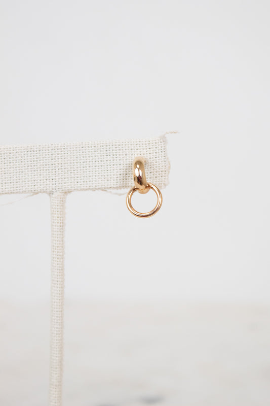 Gold ring hanging from a beige fabric strip on a light gray background