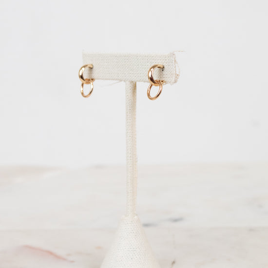 Gold earrings on a white earring stand with a marble background