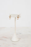 Gold earrings on a white earring stand with a marble background