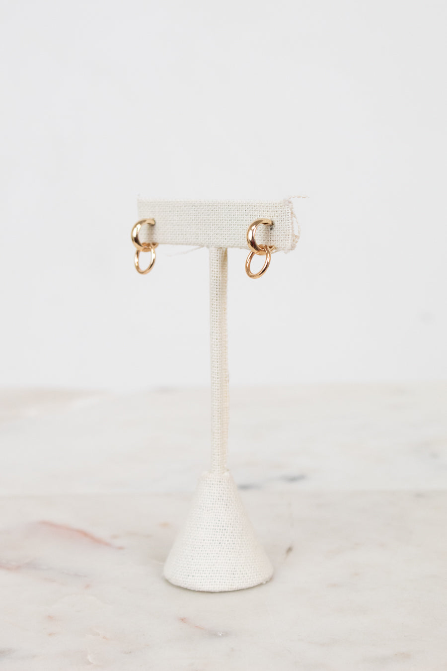 Gold earrings on a white earring stand with a marble background