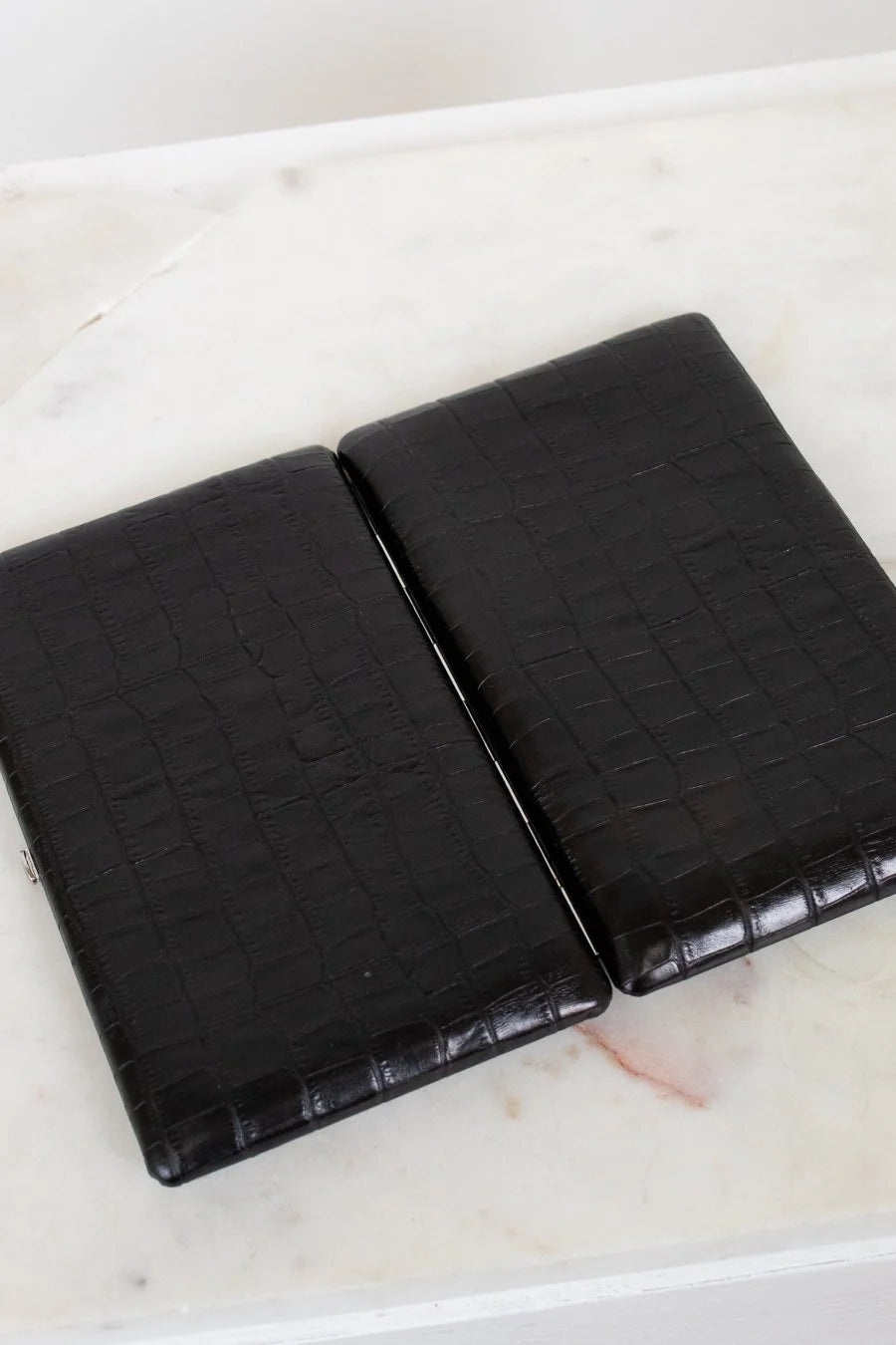 Open black crocodile-patterned wallet on a marble surface