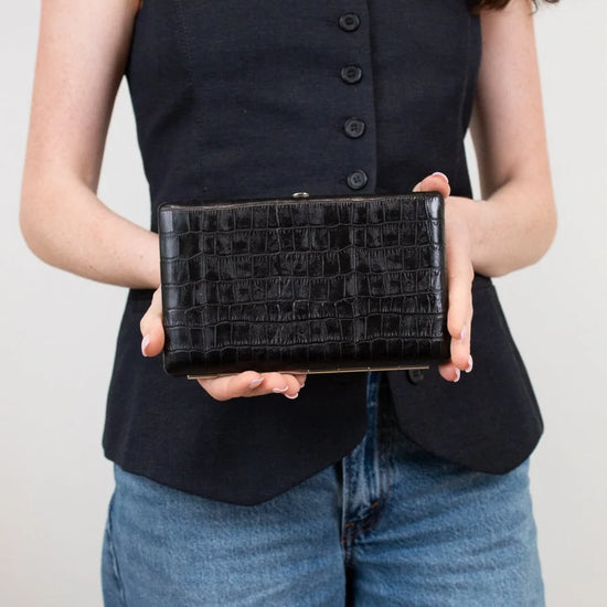 Person holding a black clutch bag against a neutral background