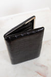 Black crocodile-patterned wallet on a light marble background