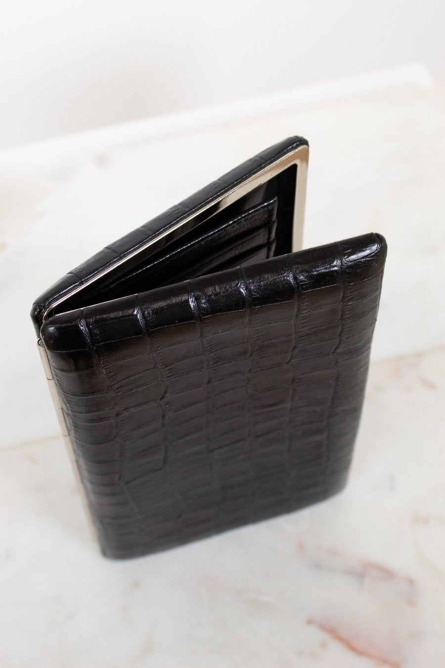 Black crocodile-patterned wallet on a light marble background