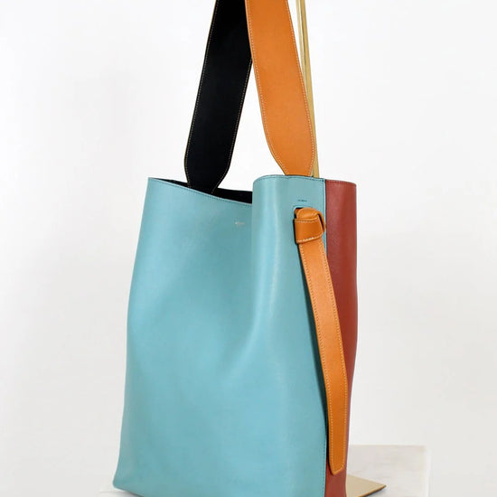 Multicolored tote bag with a blue body, orange strap, and brown handle on a white background