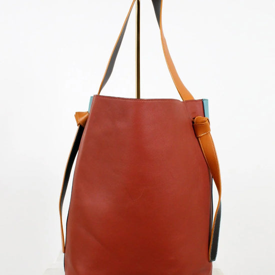 Brown leather tote bag with tan handle and strap on a white background