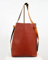 Brown leather tote bag with tan handle and strap on a white background