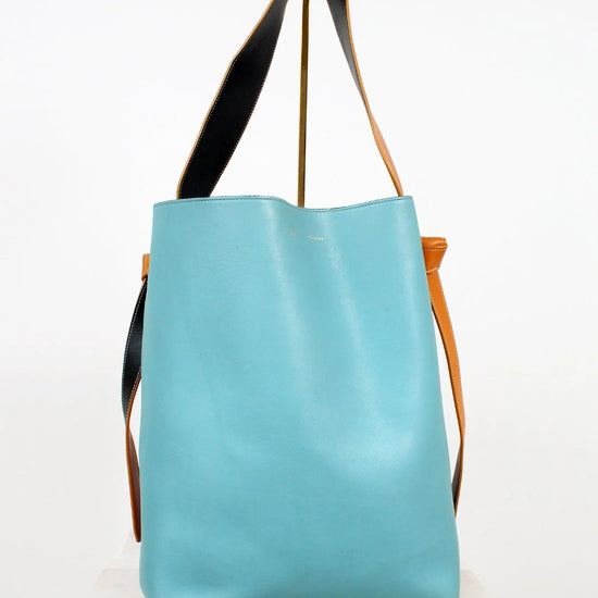 Turquoise tote bag with black and brown straps on a white background