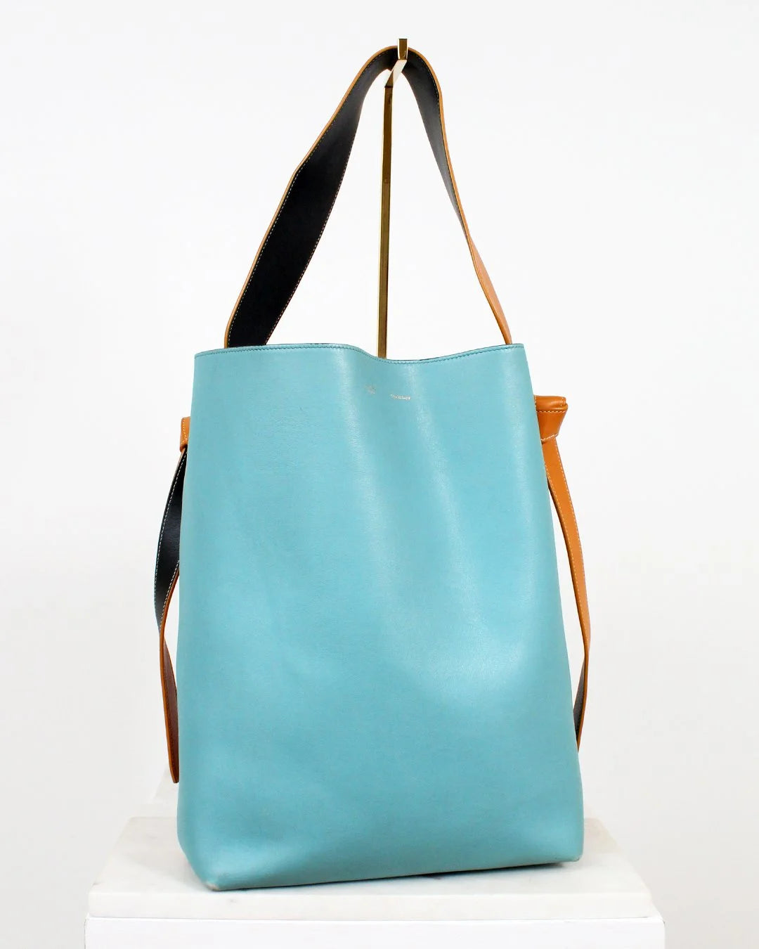 Turquoise tote bag with black and brown straps on a white background