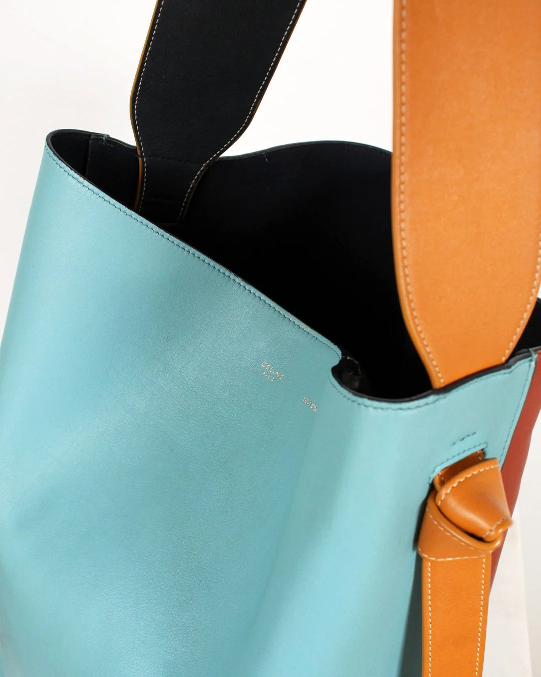 Close-up of a blue handbag with brown straps on a white background
