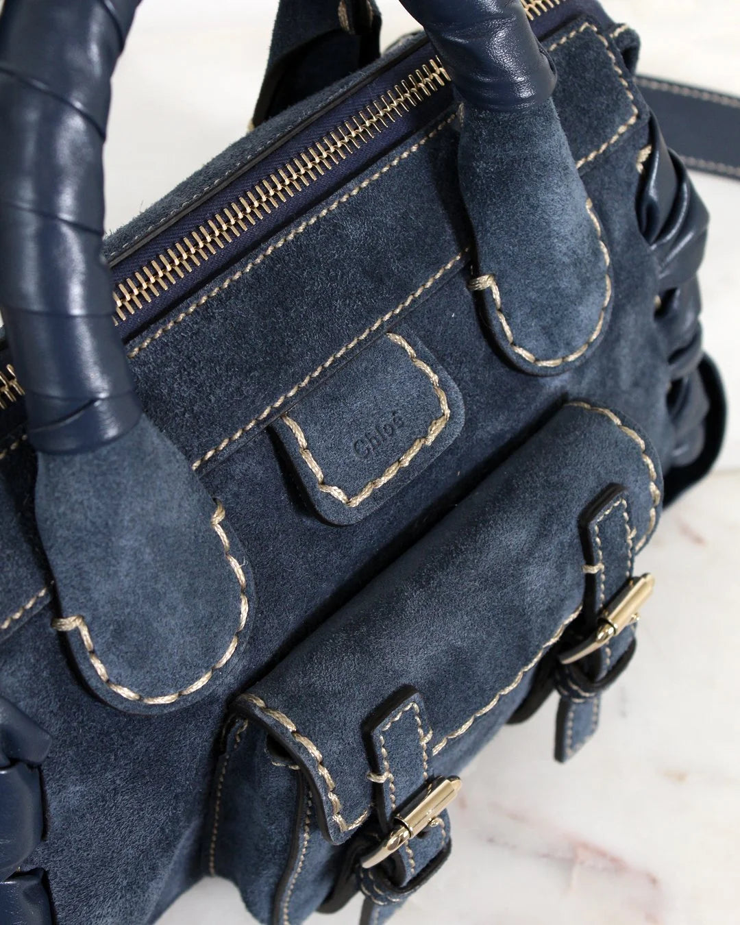 Close-up of a blue textured handbag with contrast stitching accents on a white background