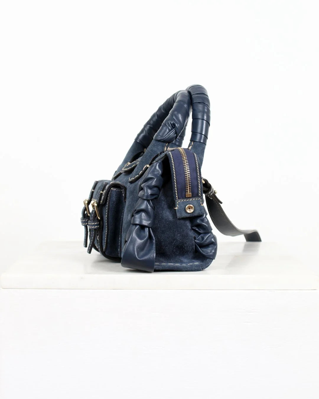 Blue leather handbag with ruched details on a white background