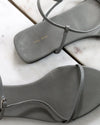 Gray sandals with 'The Row' branding on a marble surface