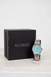 Movado watch with blue face and silver case next to a black Movado box on a white background