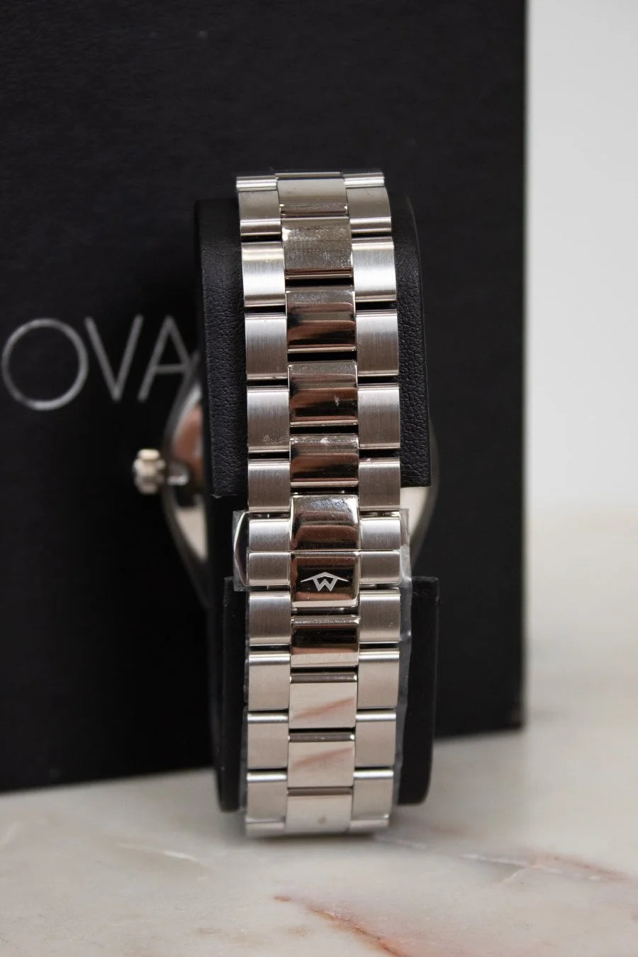 Close-up of a silver watch band on a black background with 'Oval' branding.