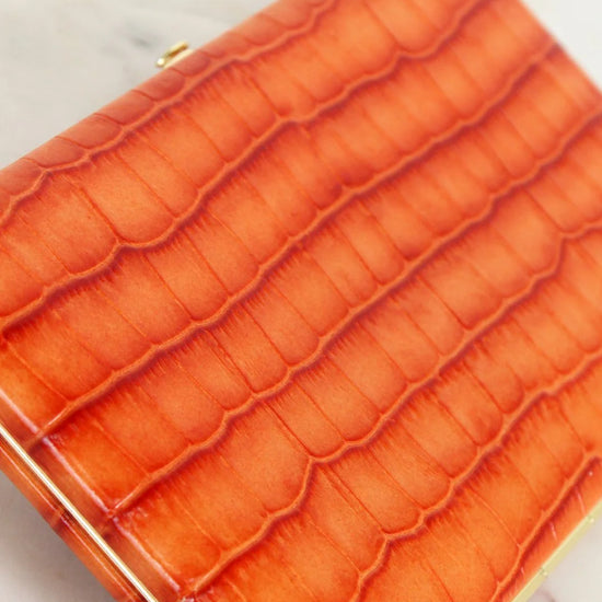 Close-up of an orange crocodile-patterned wallet on a light background