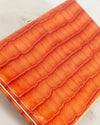 Close-up of an orange crocodile-patterned wallet on a light background