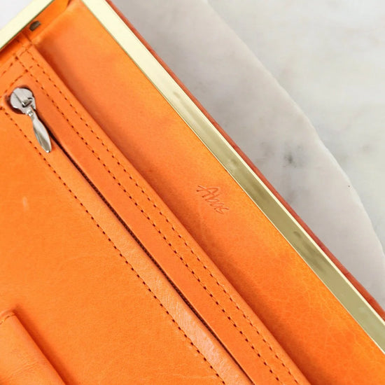 Close-up of an orange leather wallet with gold zipper and visible brand logo.