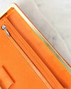 Close-up of an orange leather wallet with gold zipper and visible brand logo.