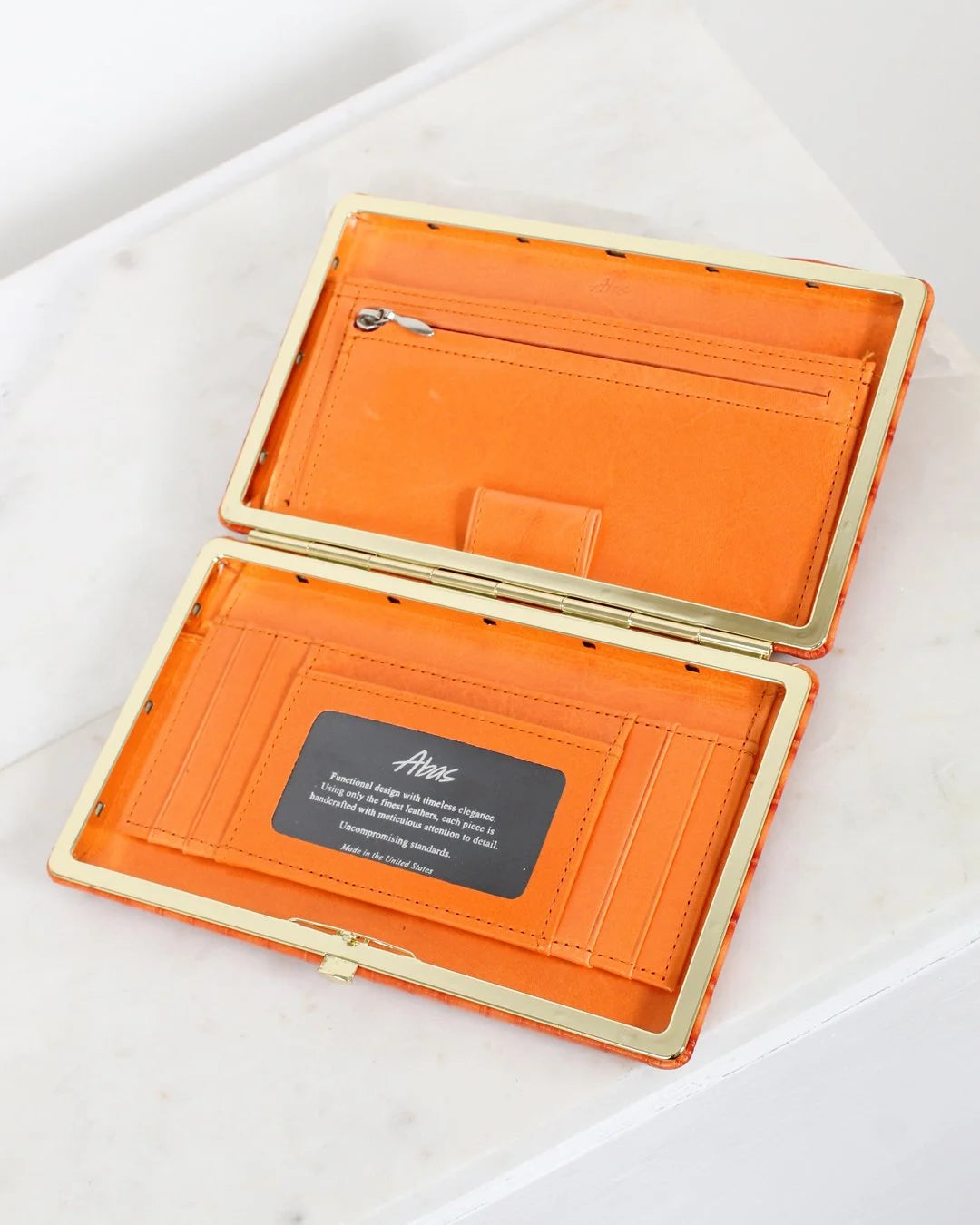 Orange wallet with gold trim on a white surface