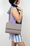 Woman holding a gray handbag against a plain background