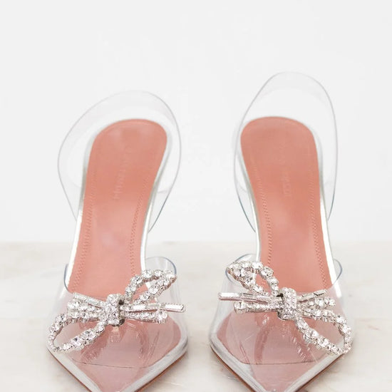 Clear high-heeled shoes with pink soles and decorative bows on a white background