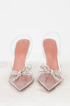 Clear high-heeled shoes with pink soles and decorative bows on a white background