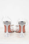 Clear high-heeled shoes with pink soles on a white background
