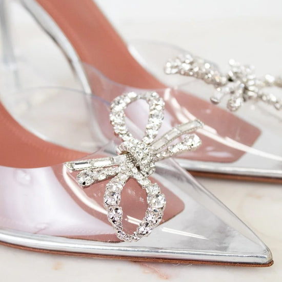 Clear high-heeled shoes with crystal bow design on a light background