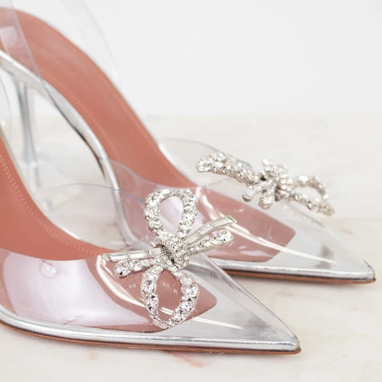 Clear high-heeled shoes with decorative bow and crystals on a light background