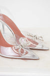 Clear high-heeled shoes with decorative bow and crystals on a light background